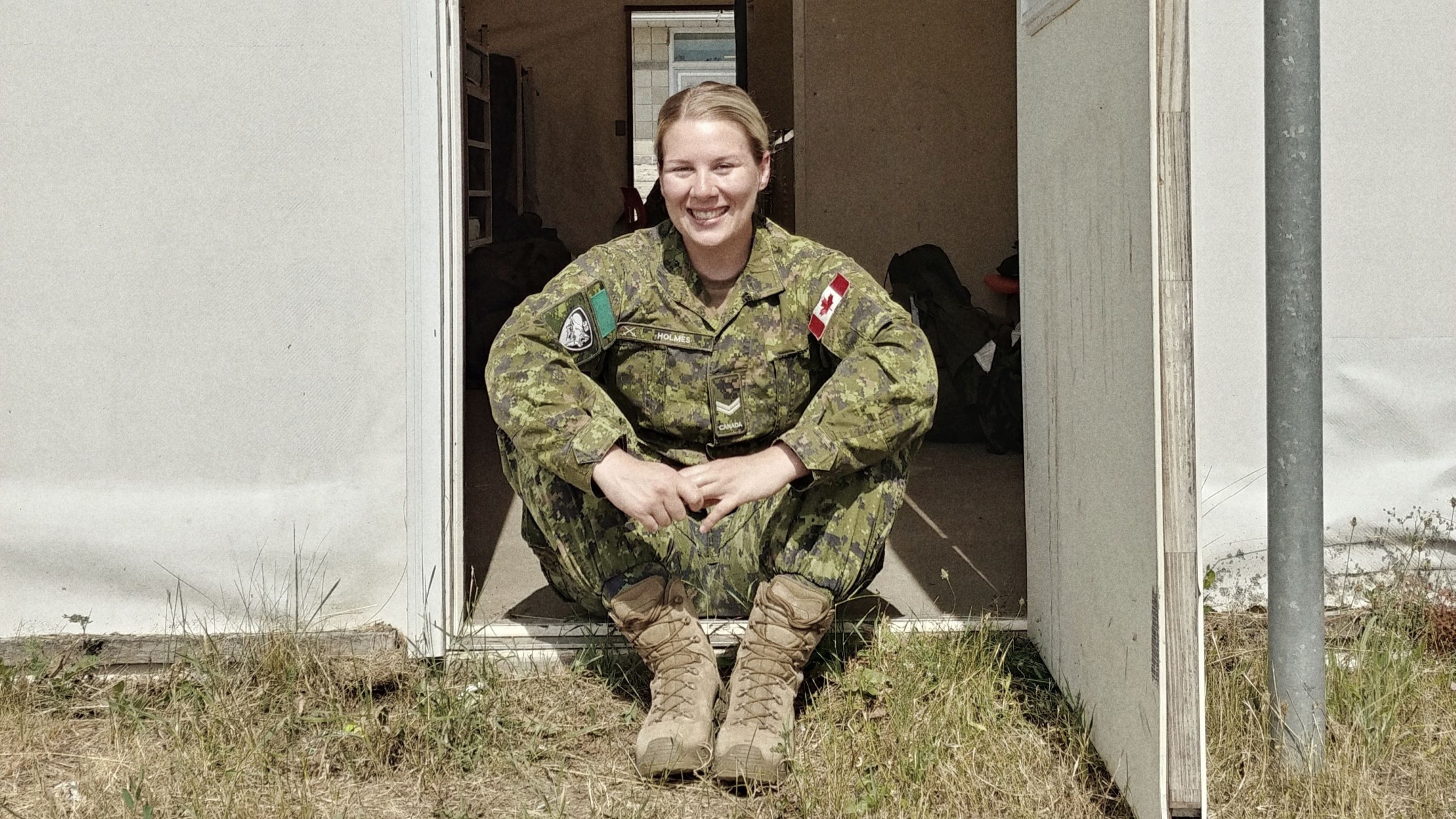 A woman in Canadian Military uniform sits in a doorway